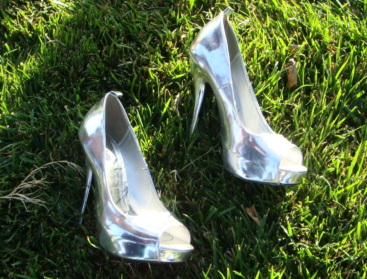 Photo of a pair of shiny, metallic silver high heels sparkling off the matte of green grass